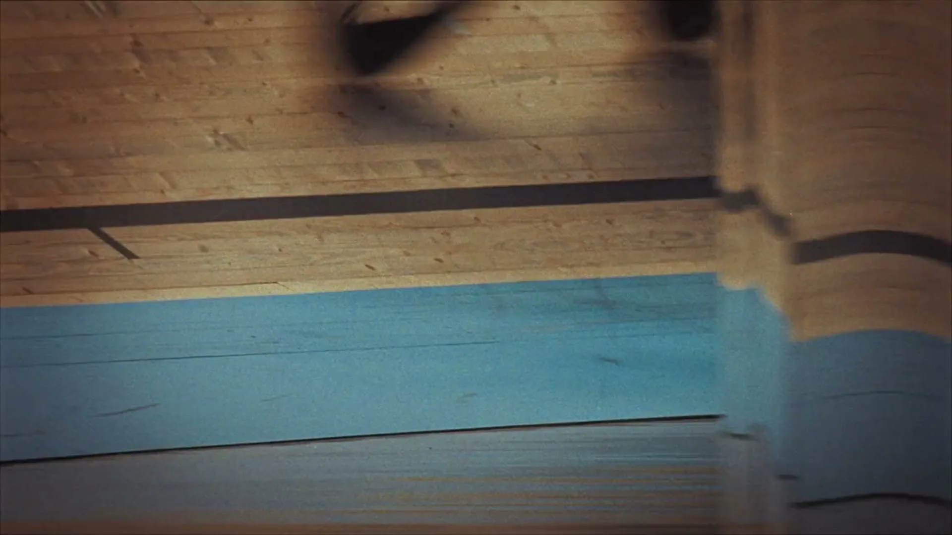 A basketball bounces on a wooden court with blue and black lines, seen from a low angle as it moves out of frame.