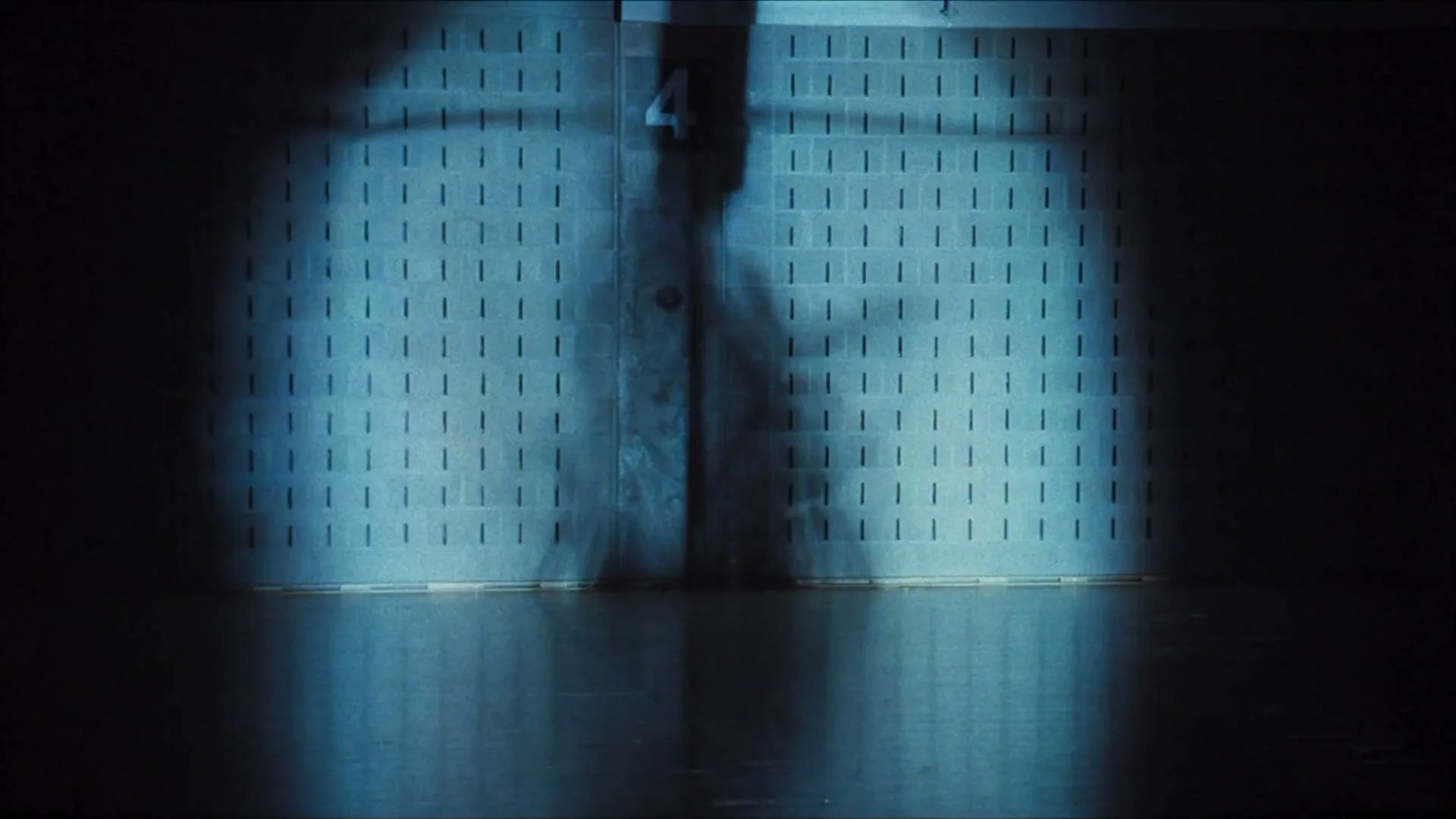 A spotlight illuminates a wall, revealing the shadow of a person with a prosthetic leg, in a dark, empty room.