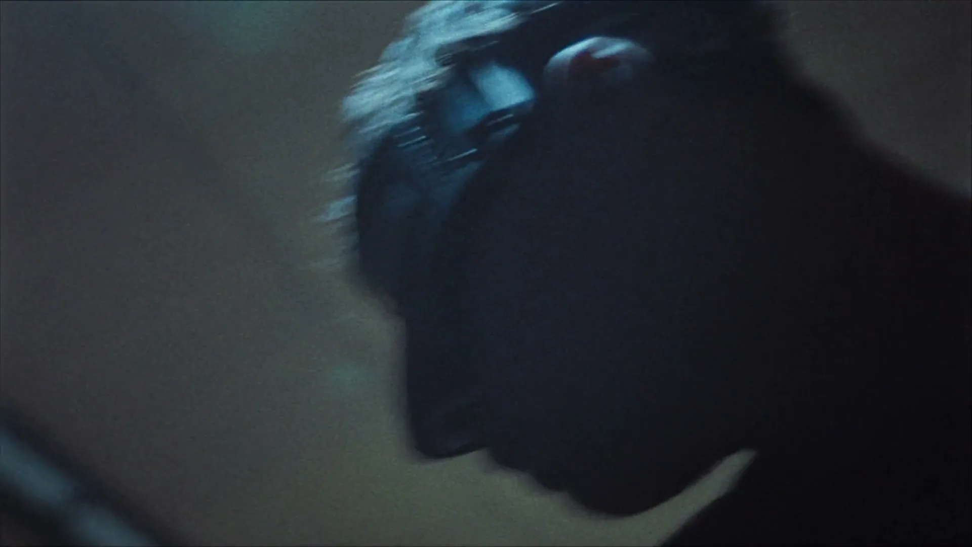 A blurry shot of a person's head, possibly a male, with dark hair and a dark object on their head, in a dark, indistinct setting.