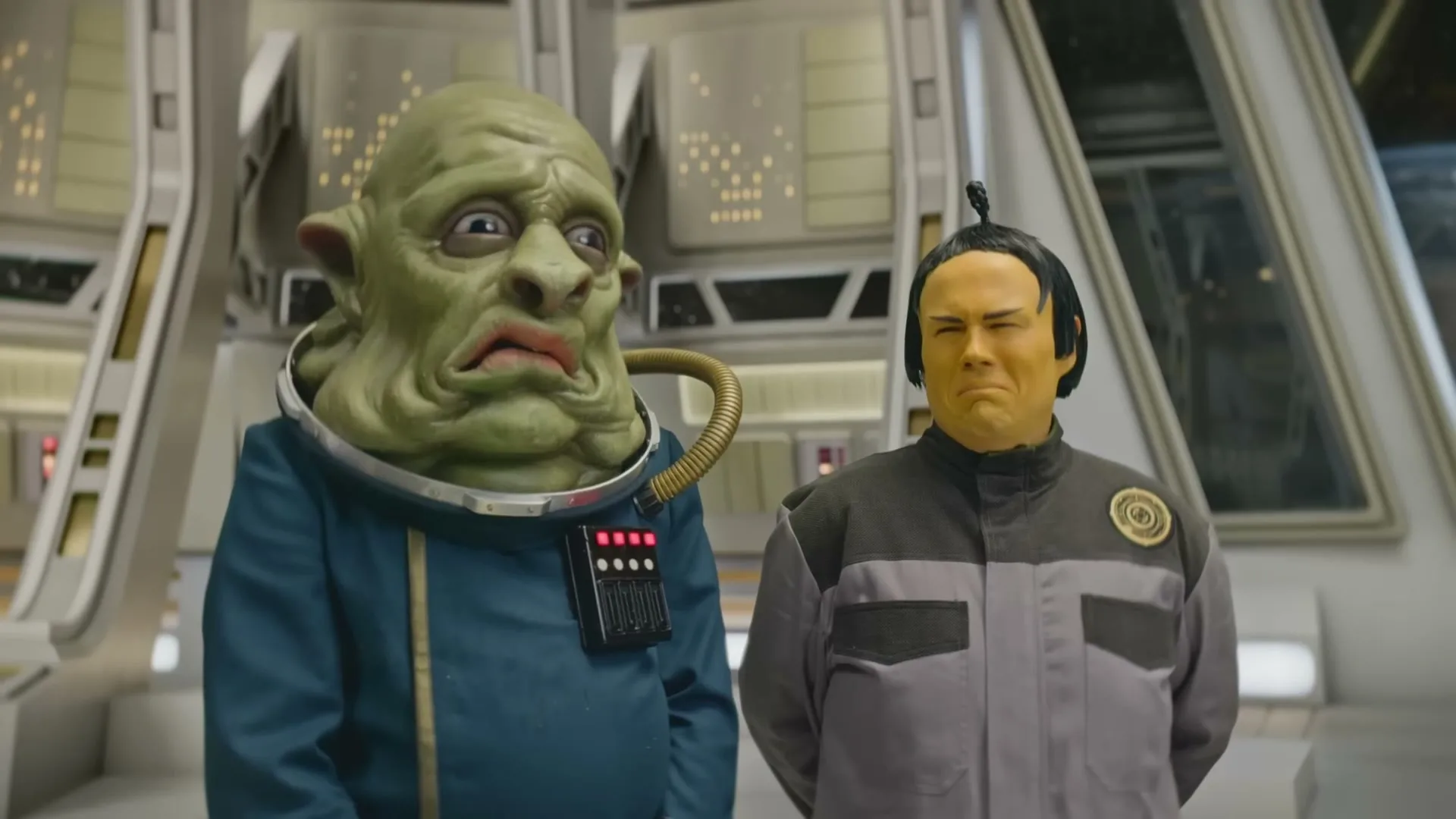 Two aliens, one green and one yellow-faced, stand side-by-side in a futuristic spaceship, both looking disgusted.