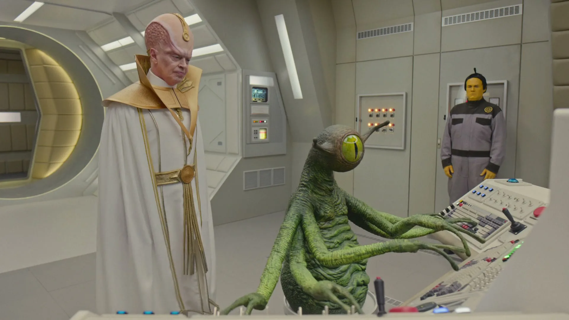 Three aliens in a spaceship control room, one in white robes, one green and multi-limbed at a console, and one yellow-skinned in a grey uniform.