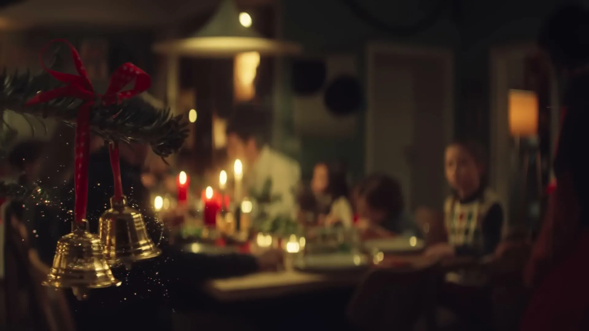 A blurry shot of a family gathered around a candlelit dining table, with Christmas bells and pine needles in the foreground.