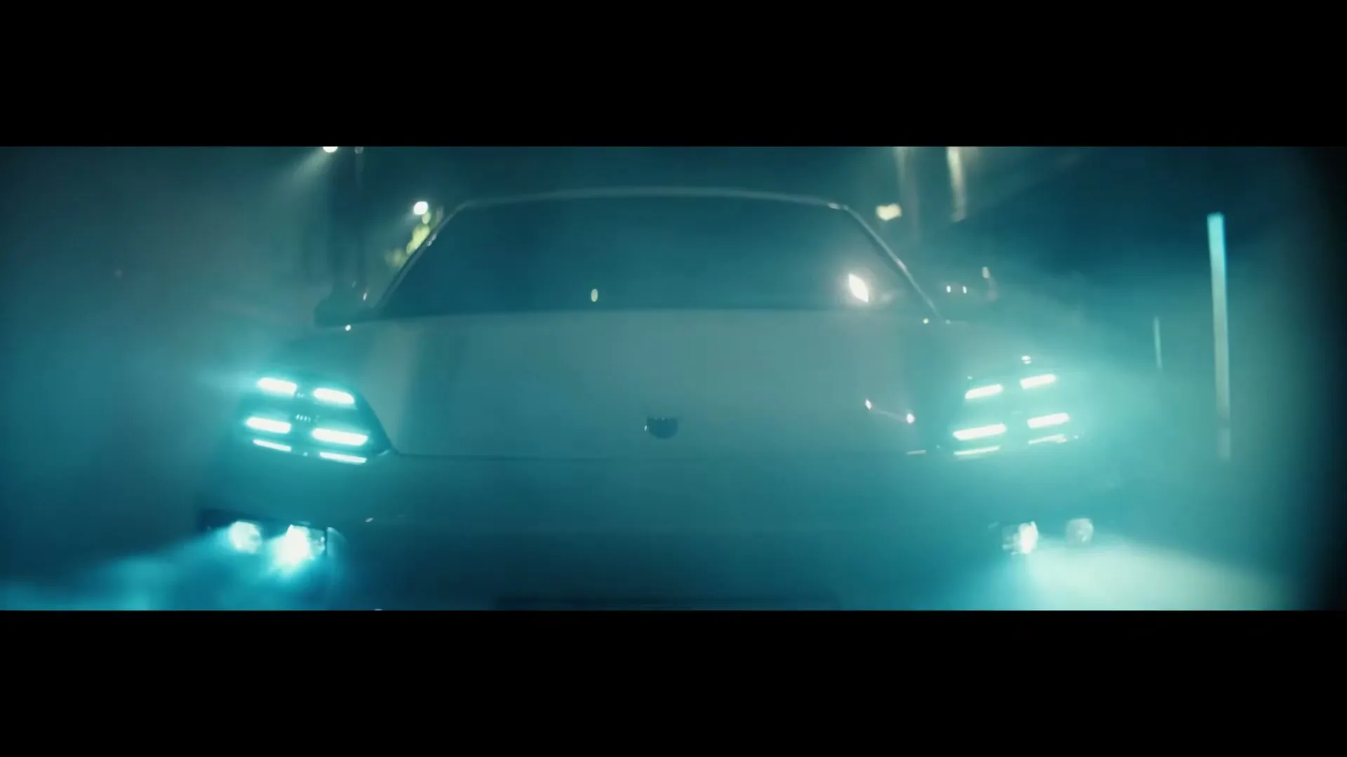 A white Porsche Macan drives towards the camera at night, its bright blue headlights illuminating the misty street.
