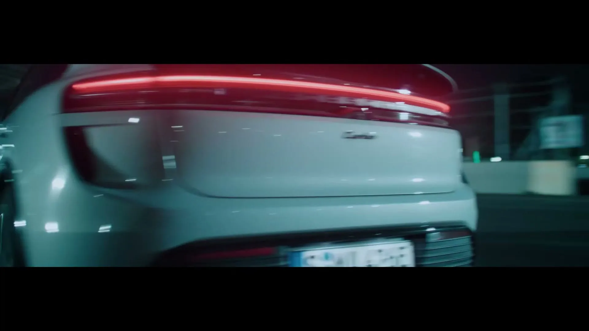 A white Porsche Macan Turbo drives at high speed on a race track at night, with bright headlights and taillights illuminating the dark surroundings.