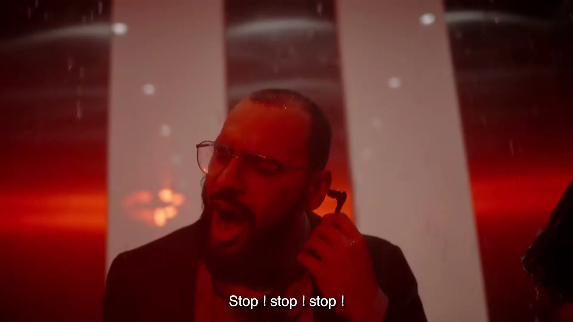 A man with a beard and glasses shouts in a red-lit, shaking elevator, trying to stop it.