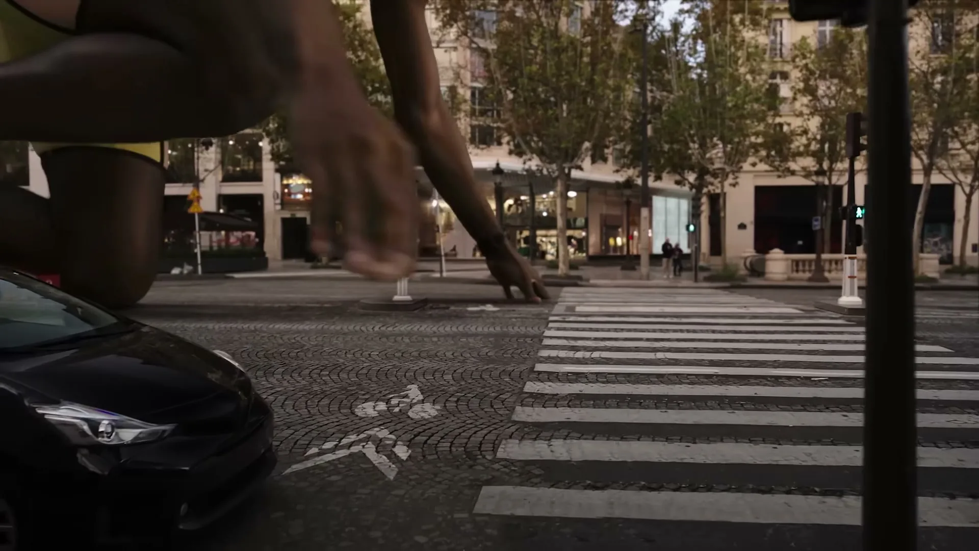 A giant male athlete in running gear crouches at a crosswalk in a city street, preparing to run.