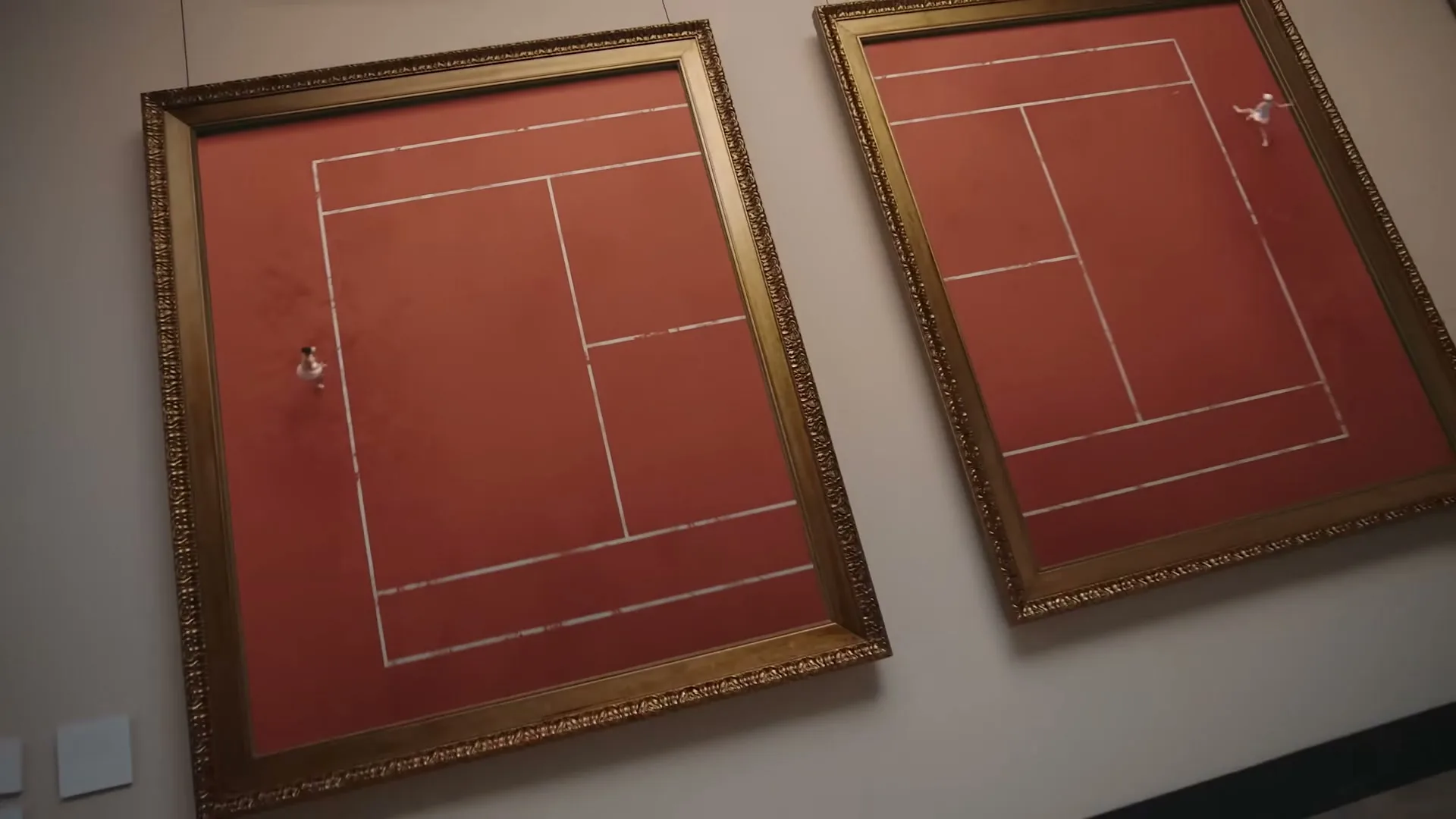 A man sits on a bench in an art gallery, looking at two framed tennis courts on the wall, where miniature tennis players are playing.