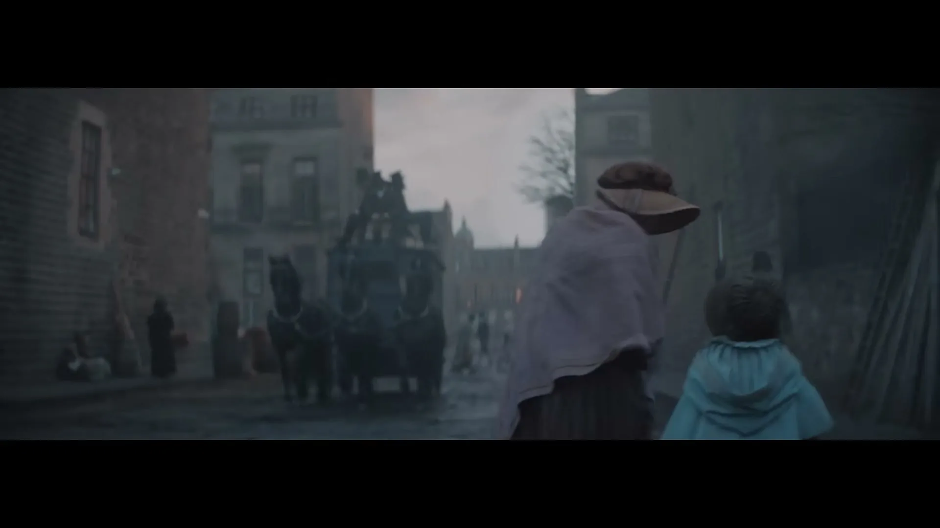 A woman in a bonnet and shawl walks with a small child in a blue cape down a cobblestone street in a historical town, with a horse-drawn carriage in the background.