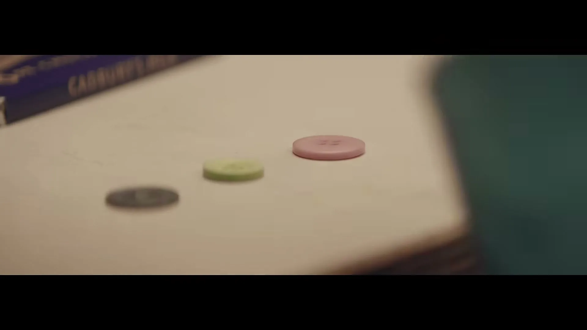 A child's hand in a teal sleeve places a pink button on a light-colored surface next to a green and a grey button.