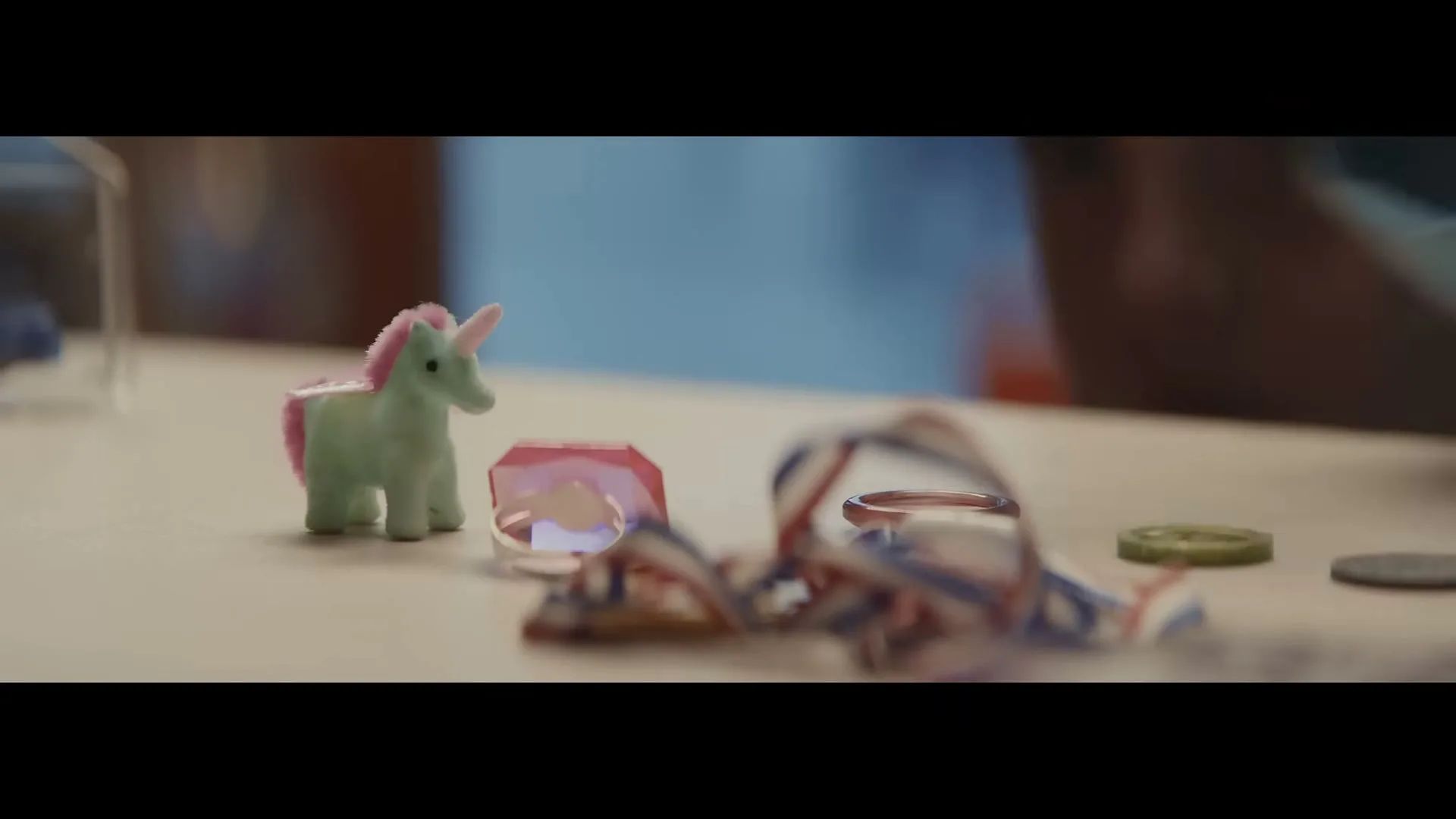A child's hand places a small green unicorn toy next to other trinkets on a light-colored surface in an interior setting.