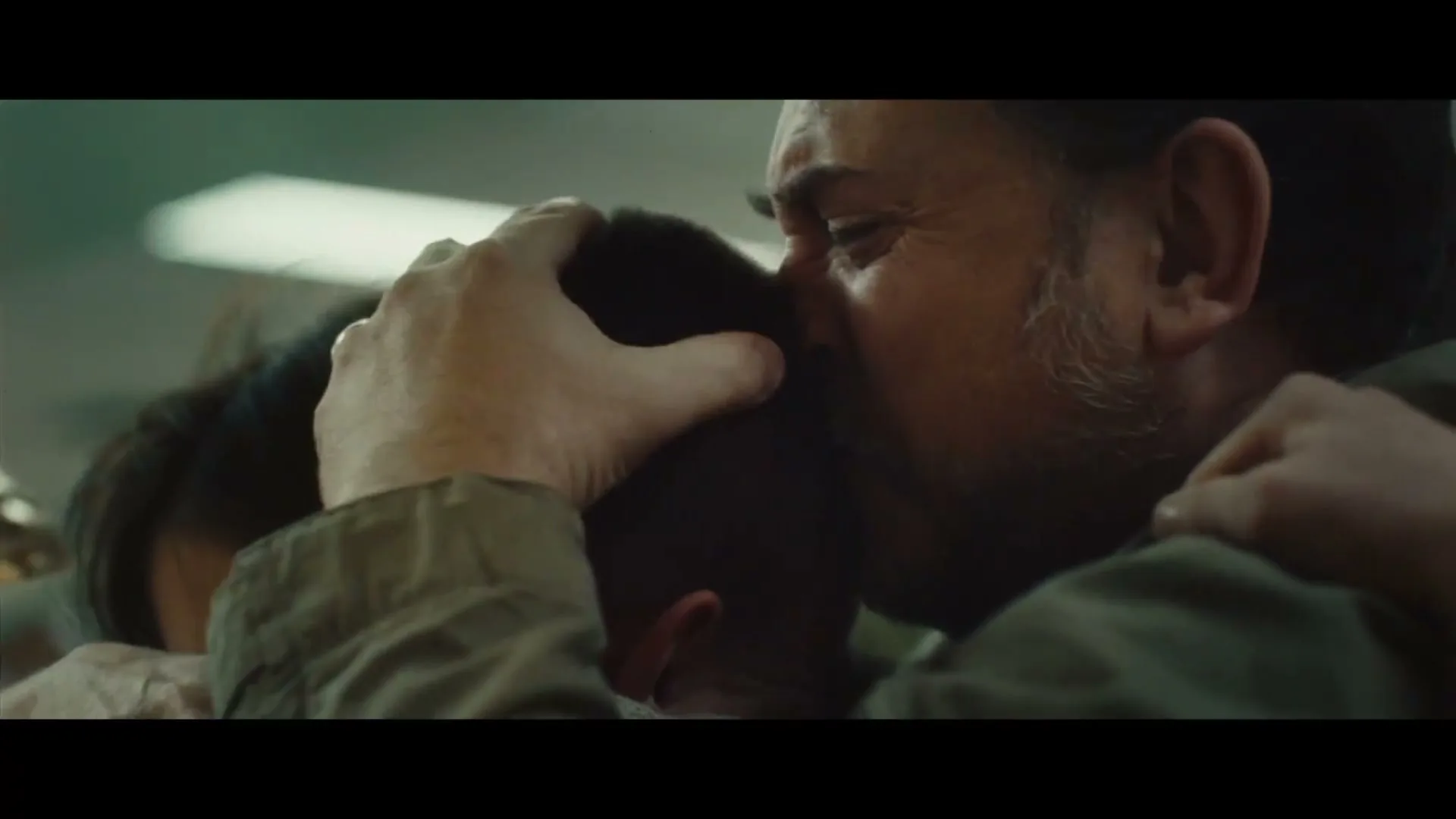 A man with a beard and a woman embrace a child, the man kisses the child's head, in an airport terminal.