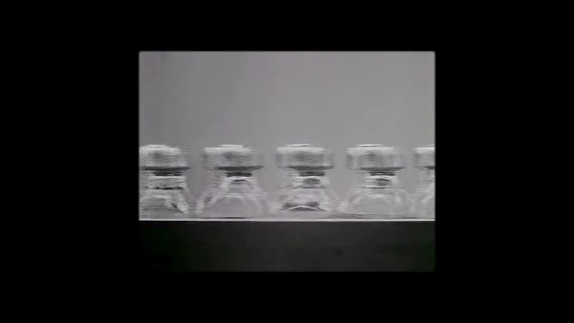 A row of small glass vials with metal caps moves from left to right on a conveyor belt in a factory setting.