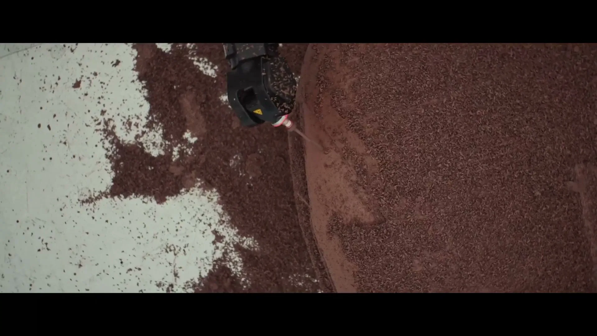 An overhead shot shows a robotic arm spraying a fine mist onto a large, circular surface covered in brown, granular material, creating a smooth texture.