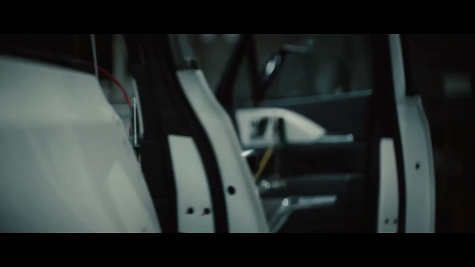 A white car's door is open, revealing the interior and some wires, in a dark, industrial setting.