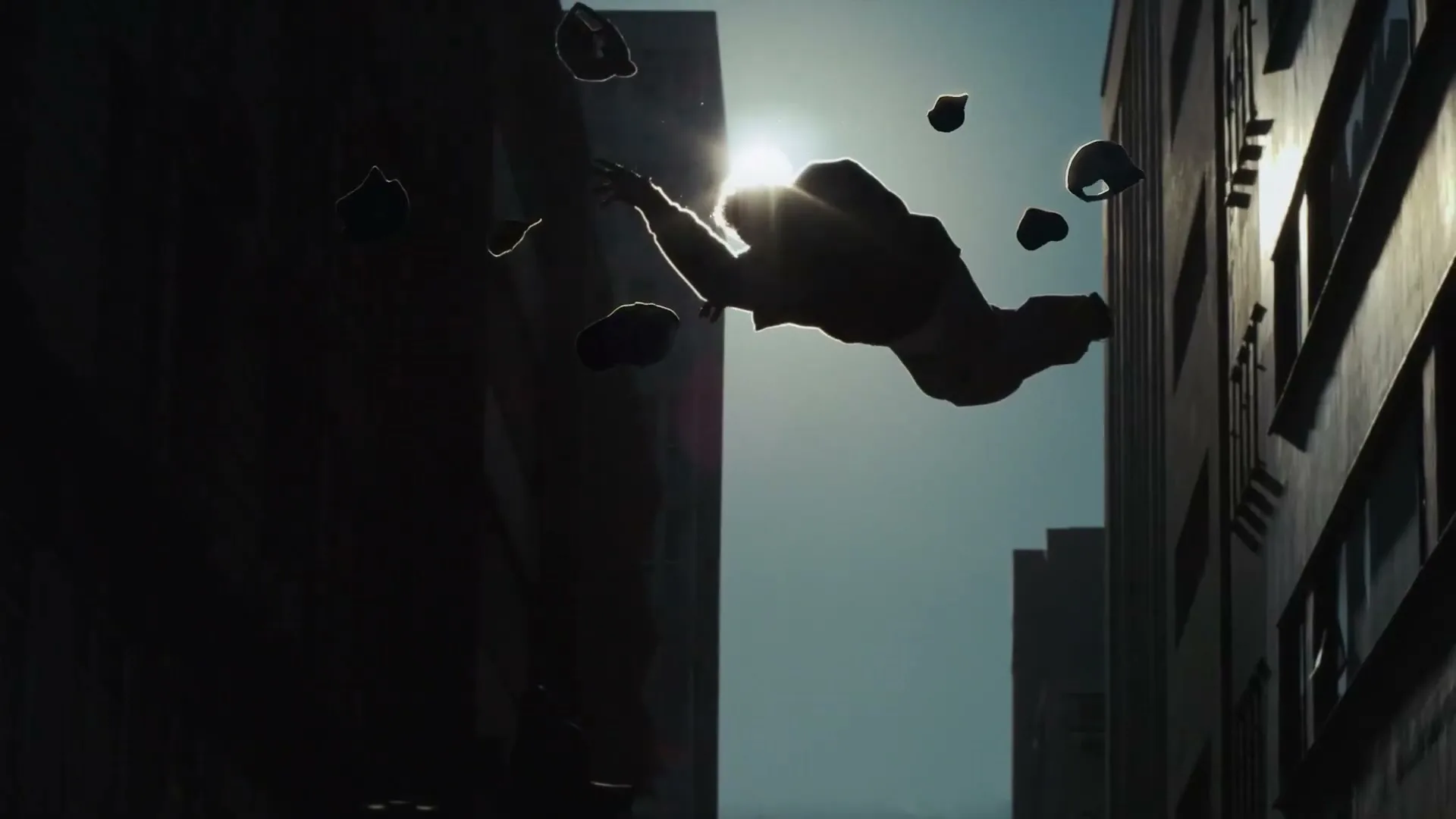 A person in silhouette falls through the air between two tall buildings, with several hats floating around them, backlit by a bright sun.