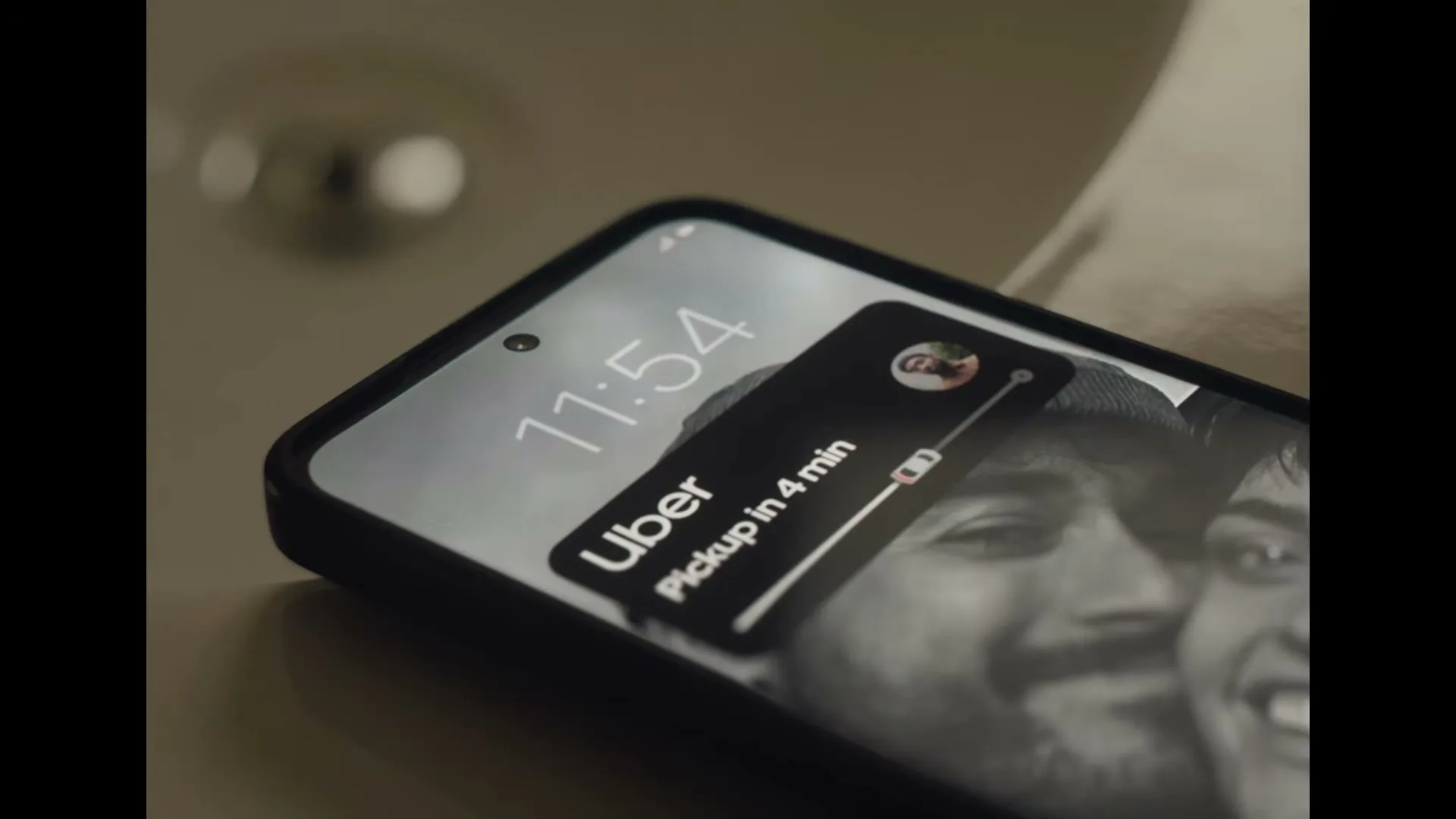 A smartphone displays an Uber notification for a pickup in 4 minutes, with a black and white photo of two smiling men as the background.