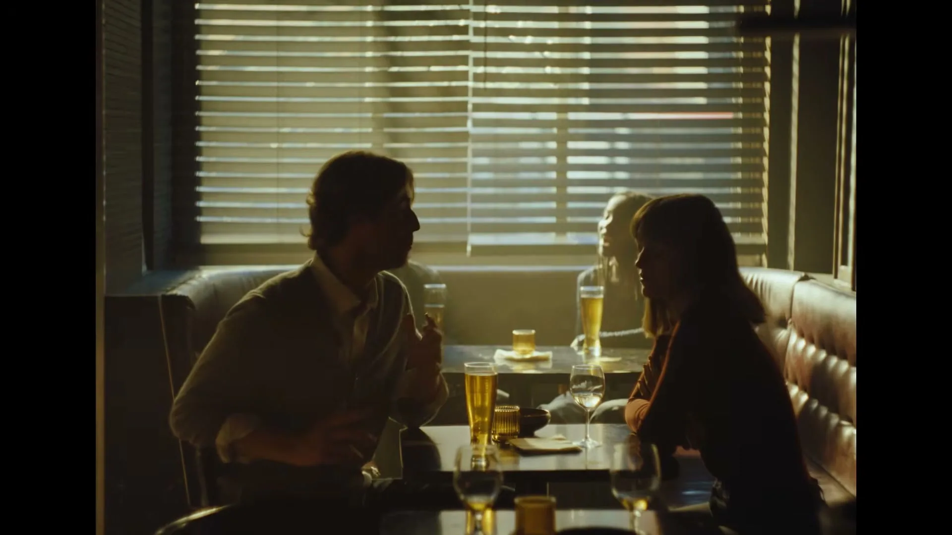 A man and a woman sit across from each other at a table in a dimly lit restaurant, talking and gesturing.