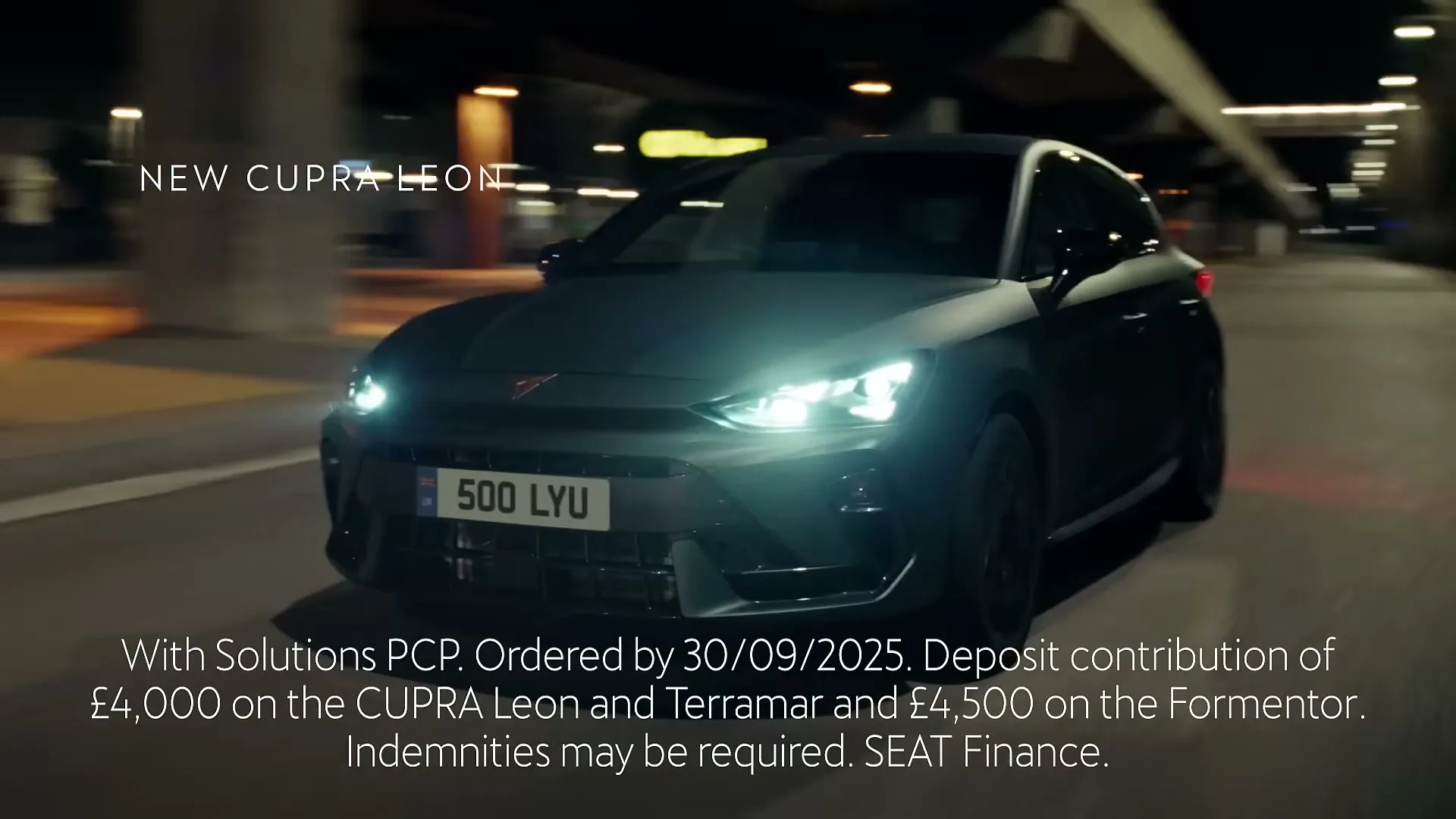 A dark grey Cupra Leon car drives on a road at night, with its headlights on, as text appears on screen.