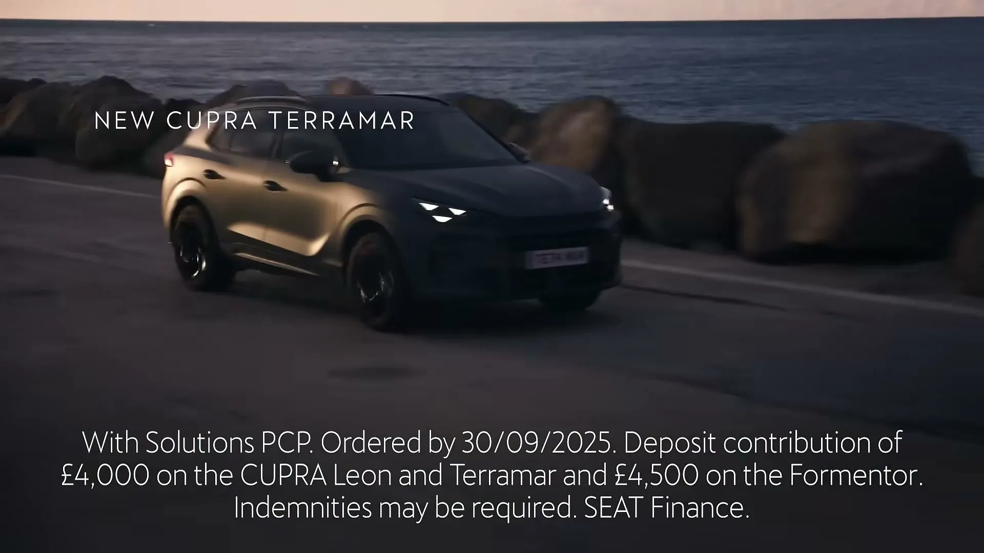 A dark grey Cupra Terramar SUV drives along a coastal road at dusk, with the ocean and rocks in the background.