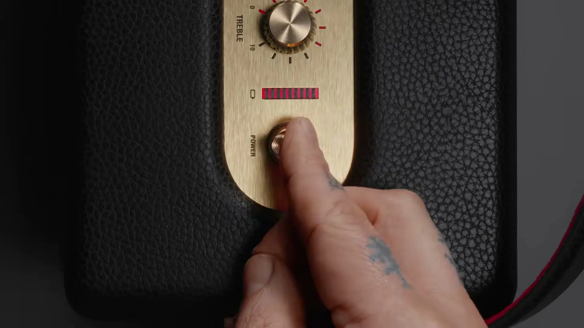 A hand with a tattoo turns the power knob on a black and gold Marshall speaker, activating a red light bar.