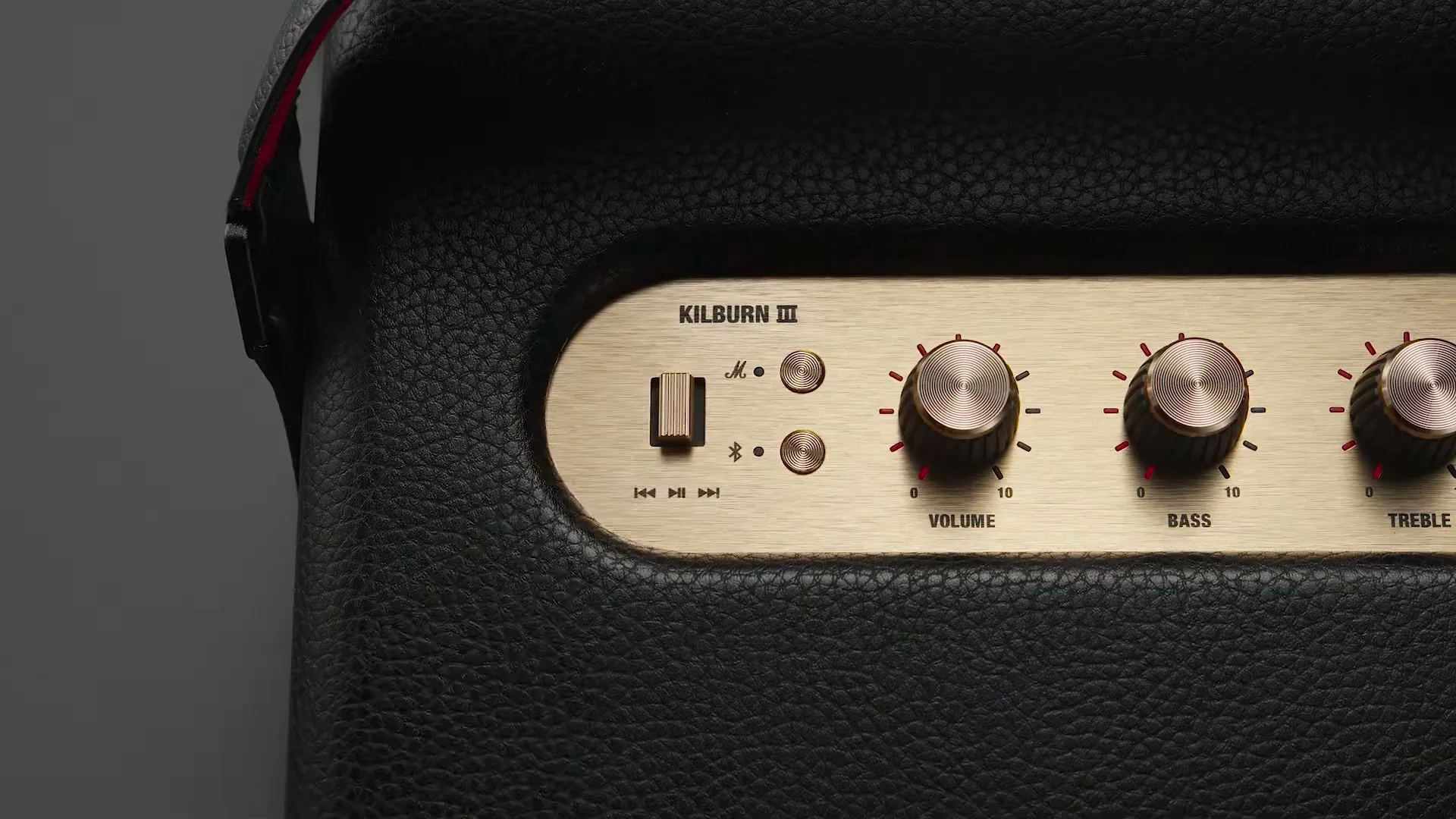 A close-up shot of a Marshall Kilburn III speaker, showing the control panel with a hand adjusting the volume knob.
