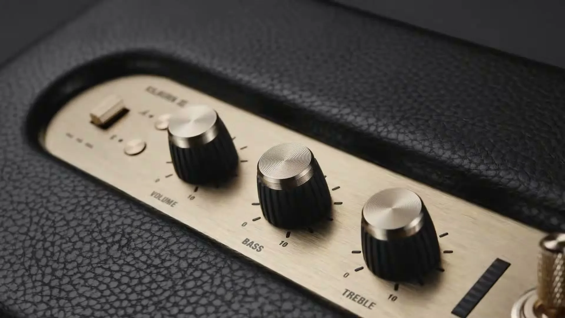 A close-up shot of the top panel of a black Marshall Kilburn III speaker, showing the gold-colored control knobs for volume, bass, and treble.