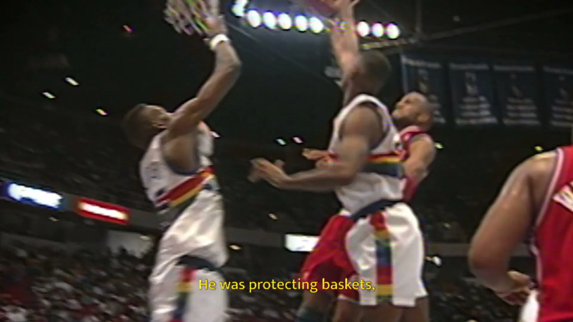 Basketball players in red and white jerseys compete on a court, one player jumps to dunk the ball into the hoop during a game.