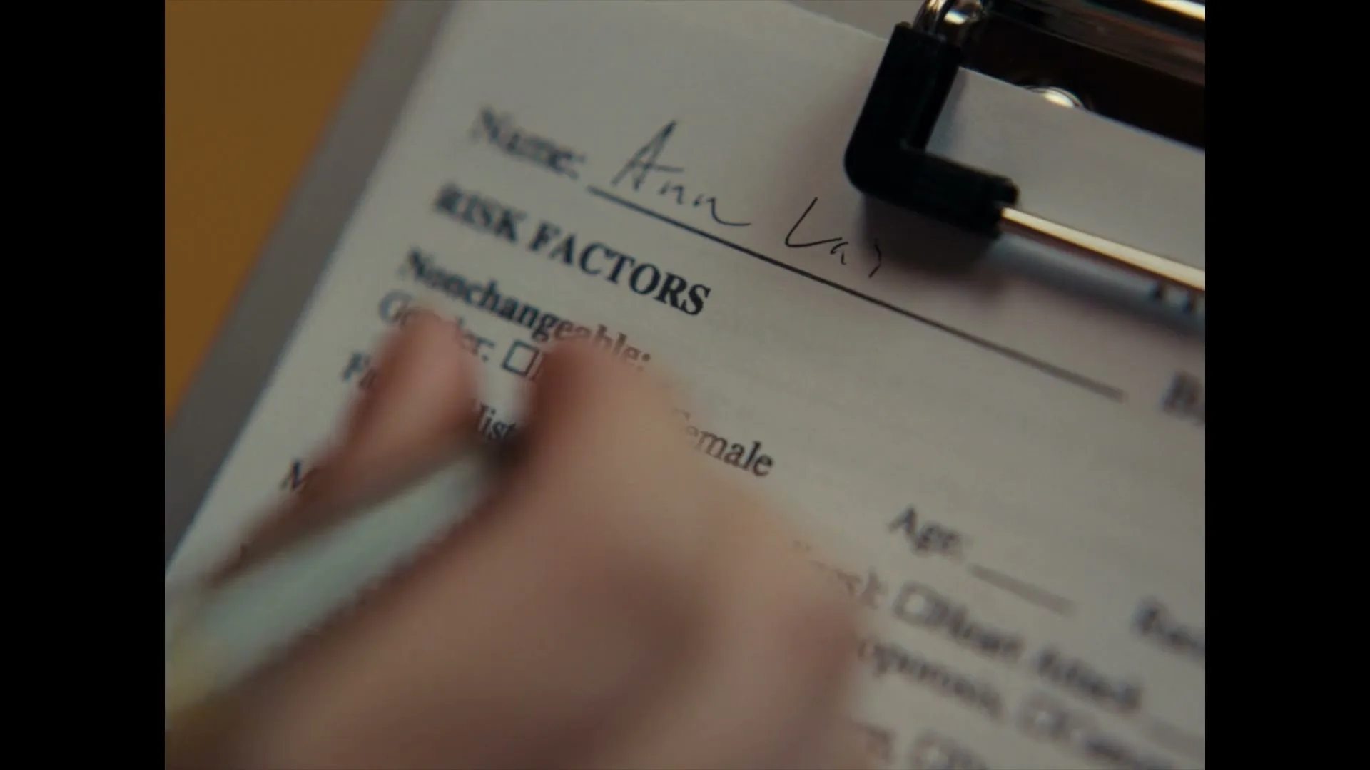 A person's hand fills out a medical form, checking the "Female" box under "Gender" and writing "Ann" for the name.