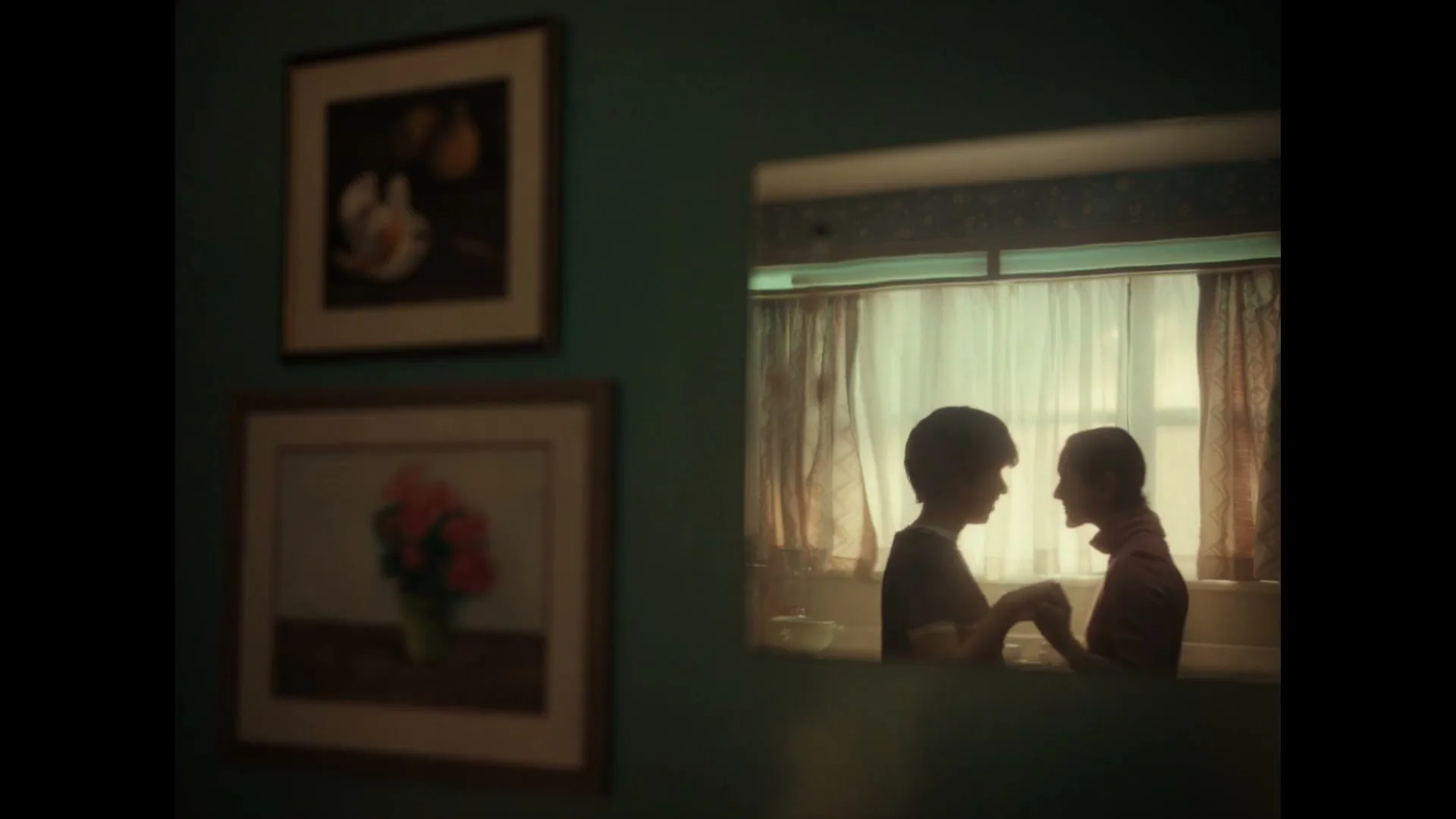 Two children, a boy and a girl, are reflected in a mirror, holding hands and looking at each other in a kitchen.