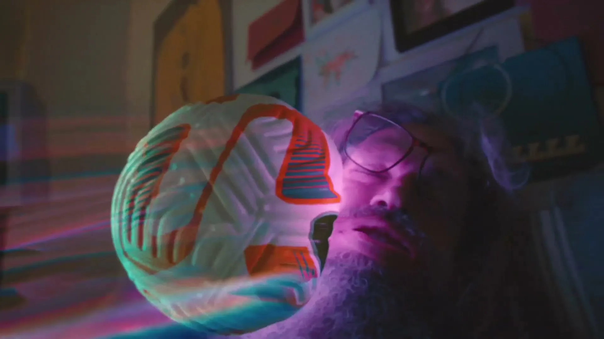 A man with a long white beard and glasses is sleeping in bed as a Nike soccer ball with colorful light trails flies past his face.