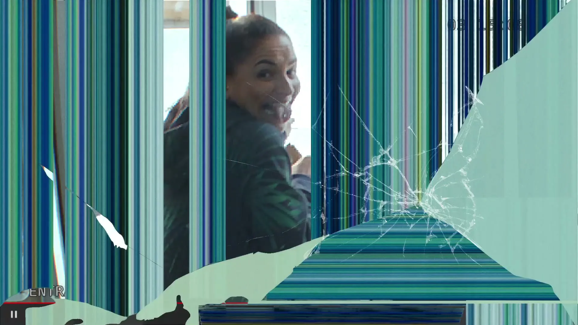 A woman with a high ponytail, wearing a green jacket, looks back and smiles mischievously while holding a paper bag, seen through a broken glass door.