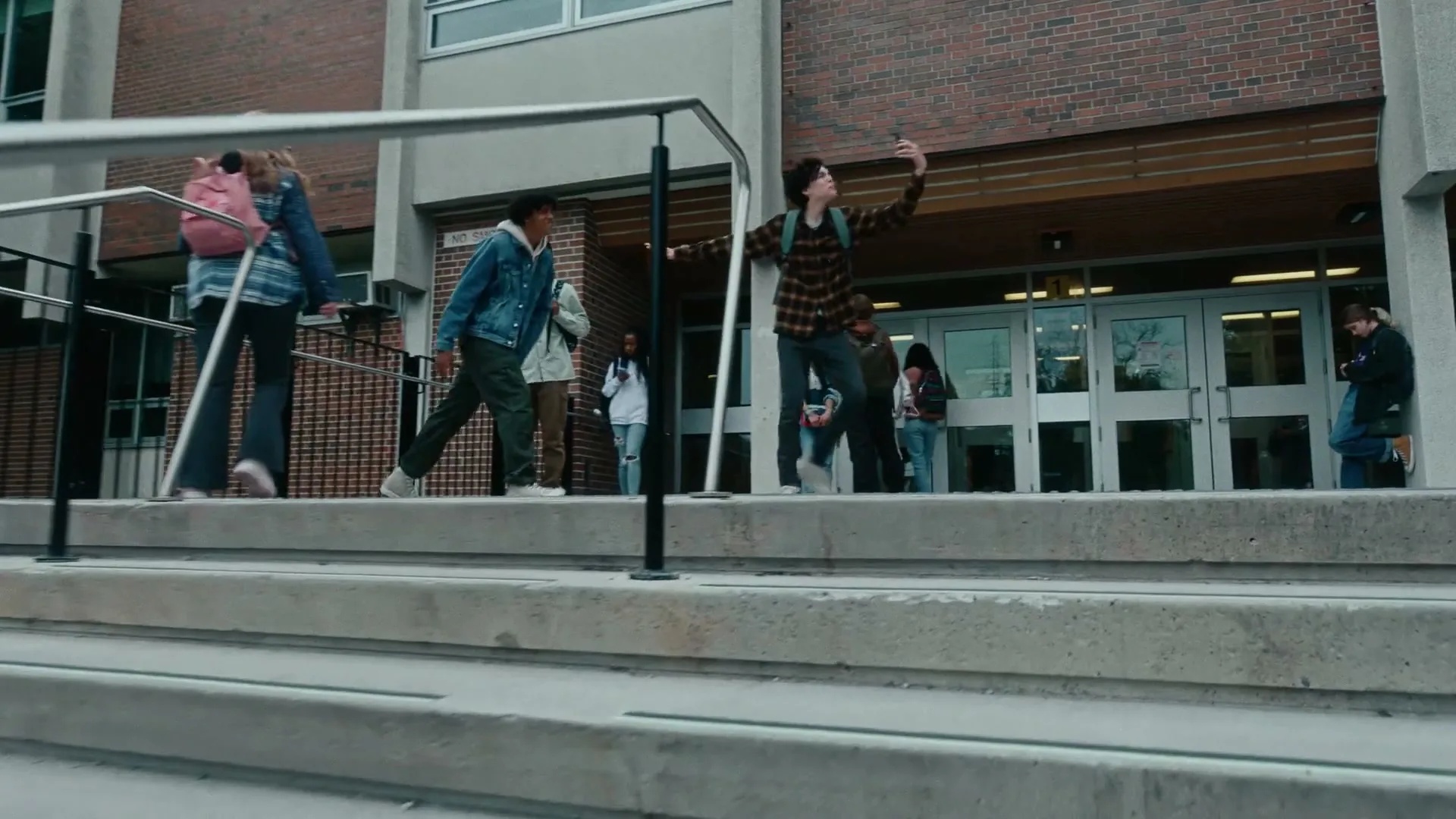 A group of diverse teenagers are walking and standing on the steps outside a school building during the day.