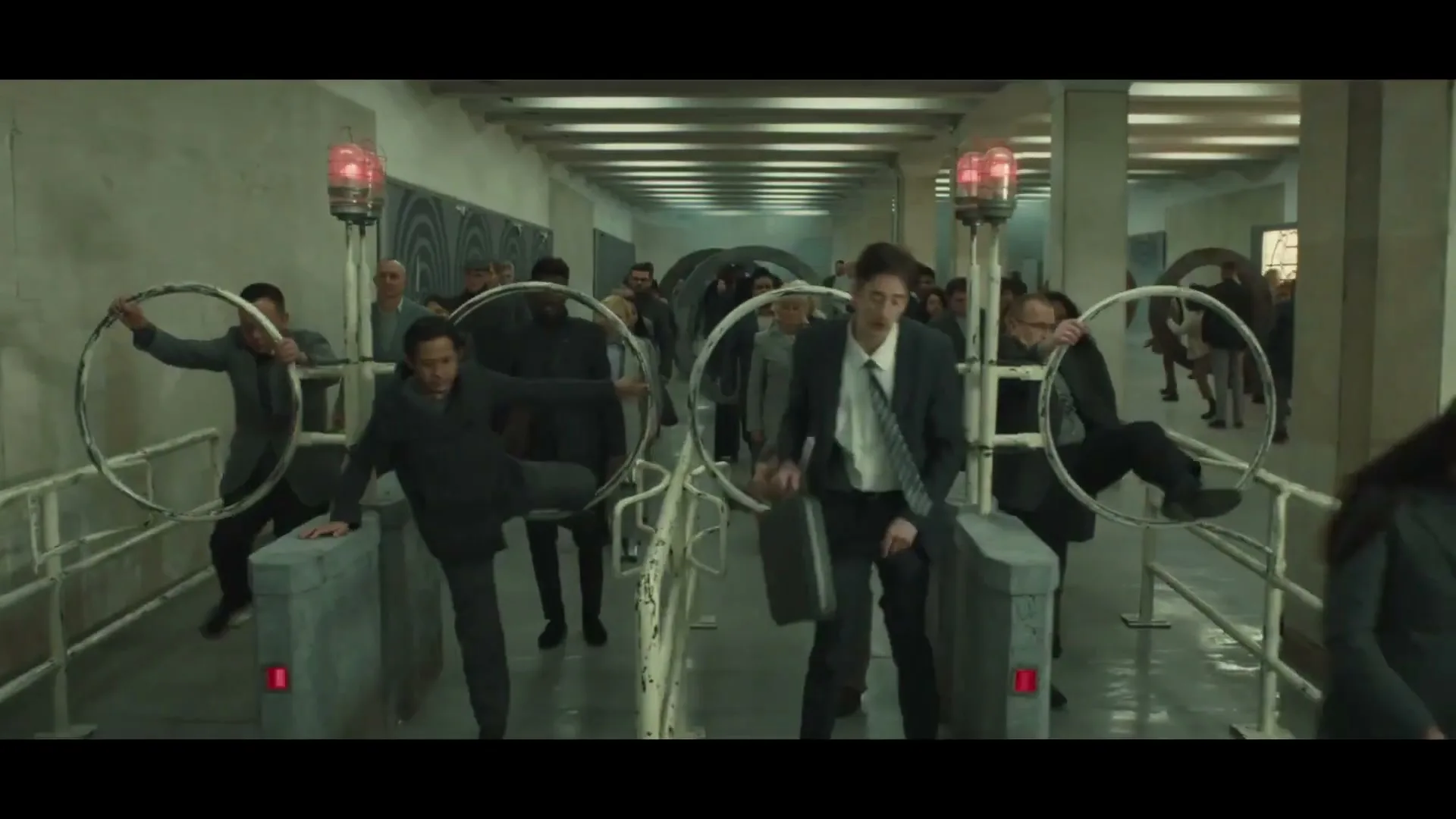 A diverse group of people in business attire struggle to pass through turnstiles with large hoops, looking frustrated in a sterile, concrete hallway.