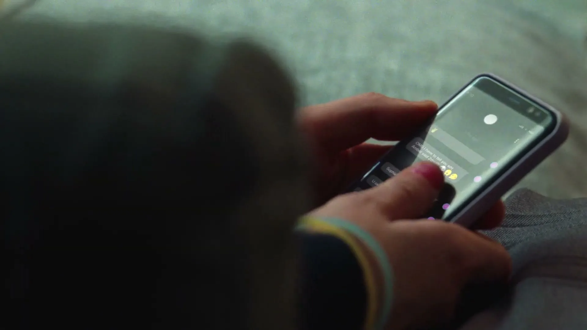 A person with painted fingernails holds a smartphone, typing a message on the screen, in a close-up shot.