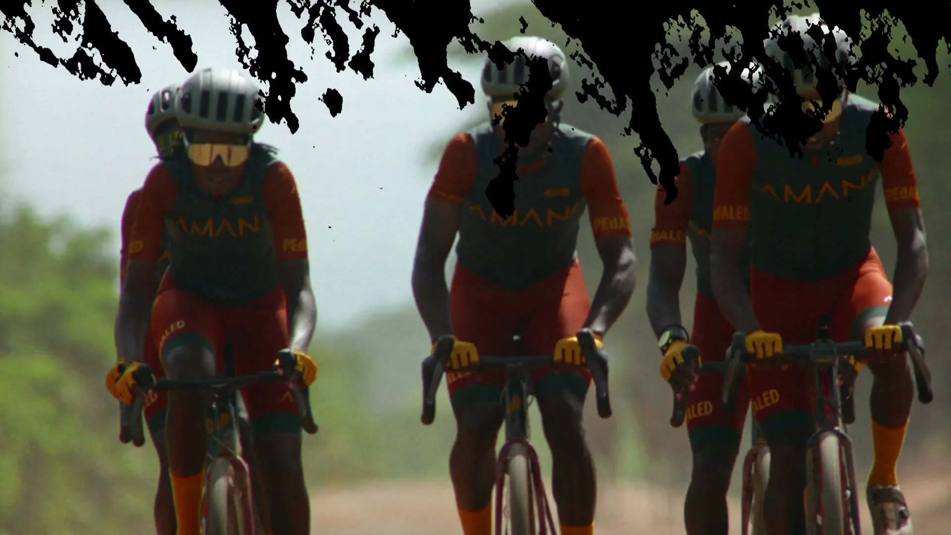 A group of five male cyclists in matching red and black uniforms with helmets and sunglasses ride their bikes on a dirt road, then the word "Amani" appears on a black screen.