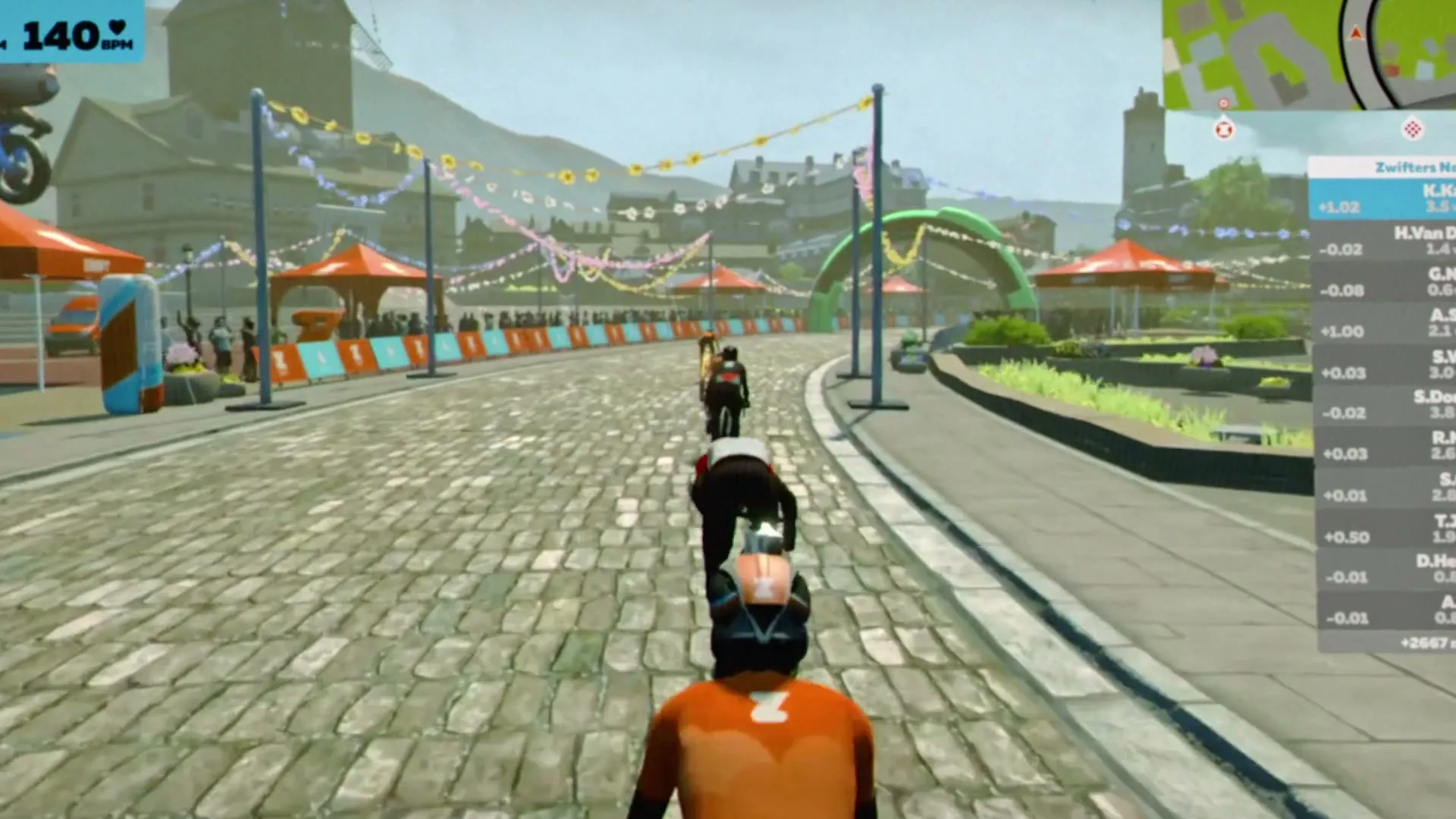 Three cyclists in racing gear ride on a cobblestone road in a virtual world, with buildings and mountains in the background.