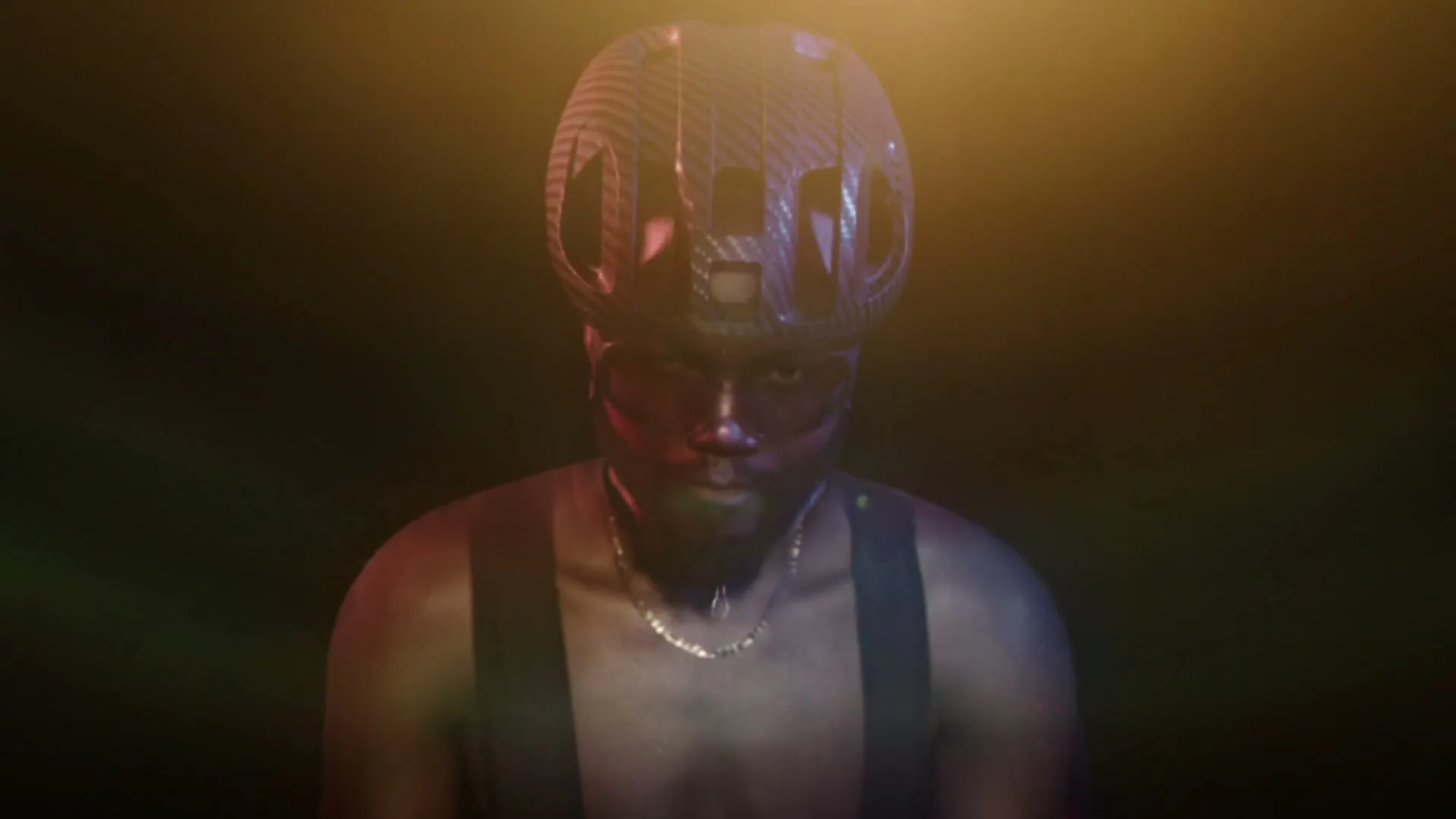 A Black man transforms into a cyclist, wearing a helmet and sunglasses, in a dark studio with colorful lighting.
