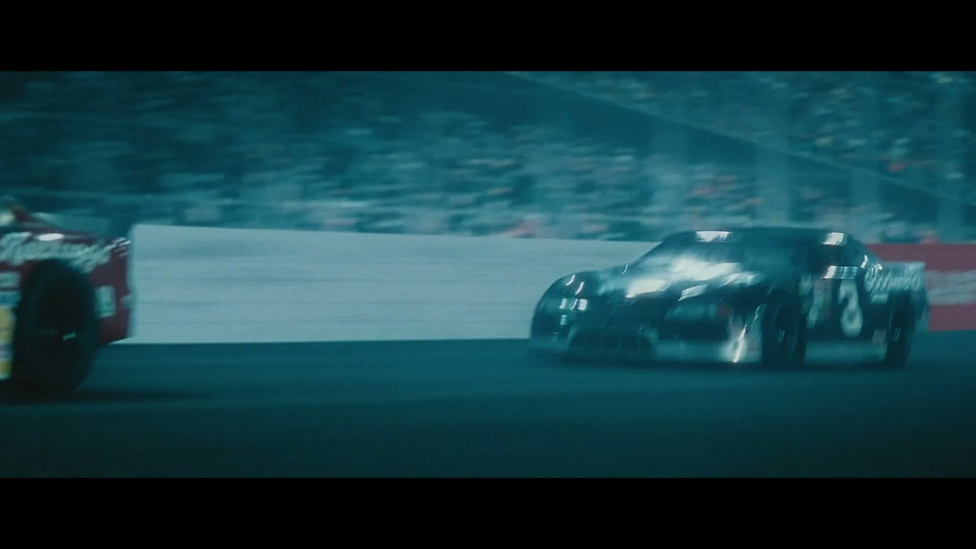Two race cars speed around a track at night, one black and one yellow, with blurred spectators in the background.