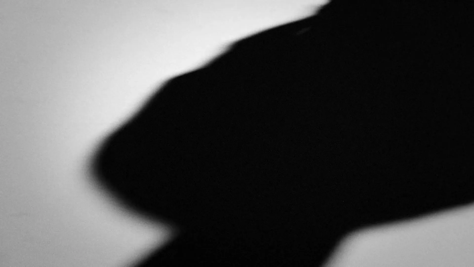A black and white shot shows the shadow of a hand moving across a light surface, creating an abstract and dynamic visual.