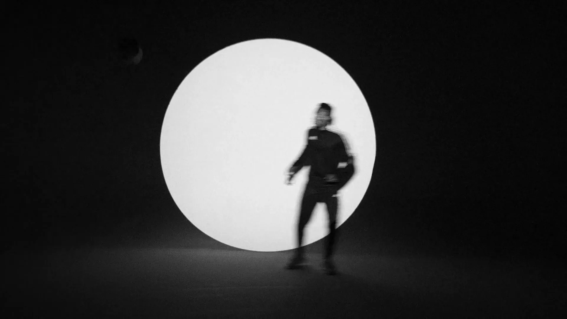A young male soccer player in a tracksuit juggles a soccer ball in front of a large white circle on a black background, then the shot quickly cuts to a blurry, grainy shot of the CN Tower in Toronto.