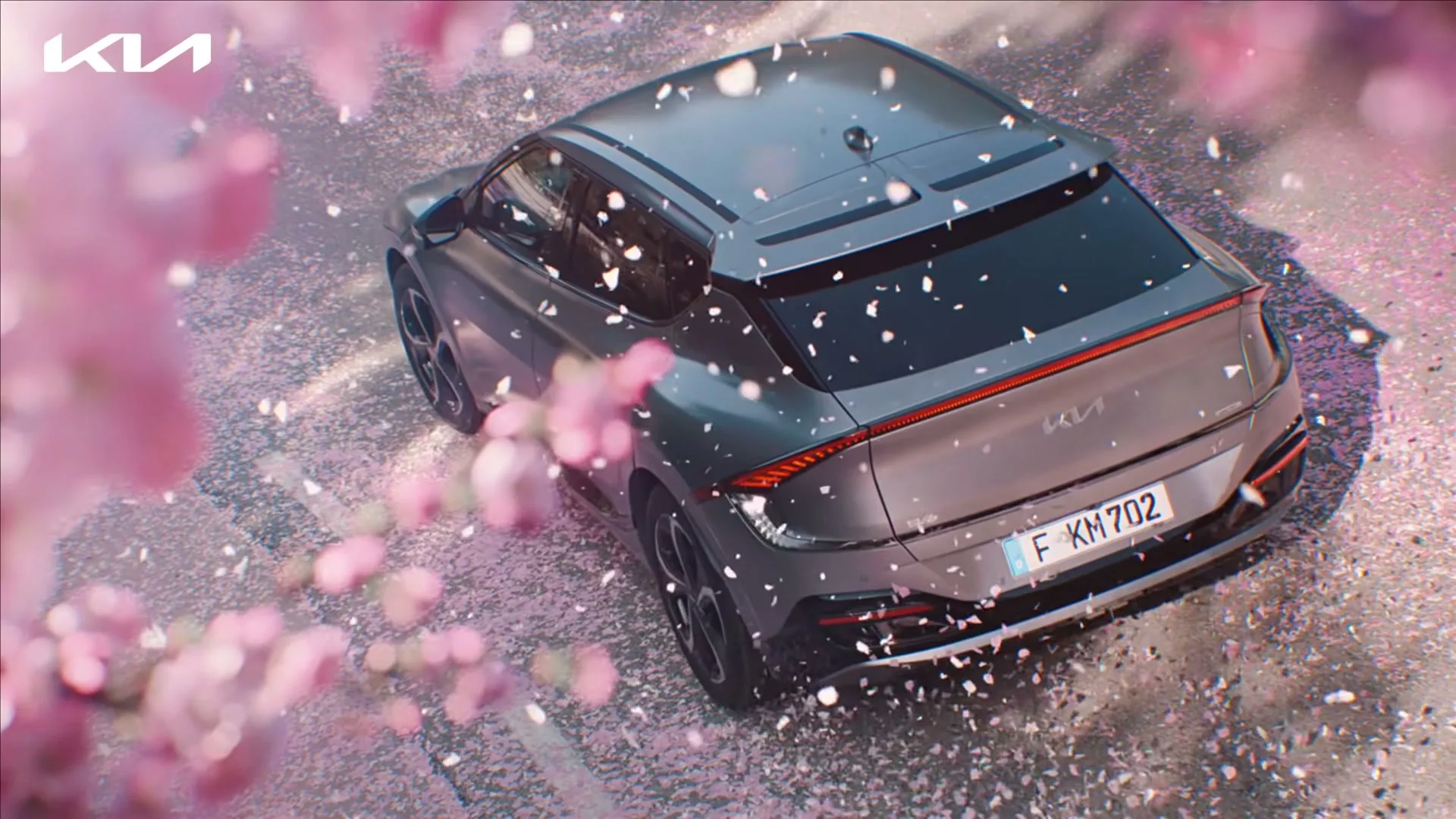 A grey Kia EV6 is seen from an overhead perspective, parked on a street covered in pink cherry blossom petals, with more petals falling.