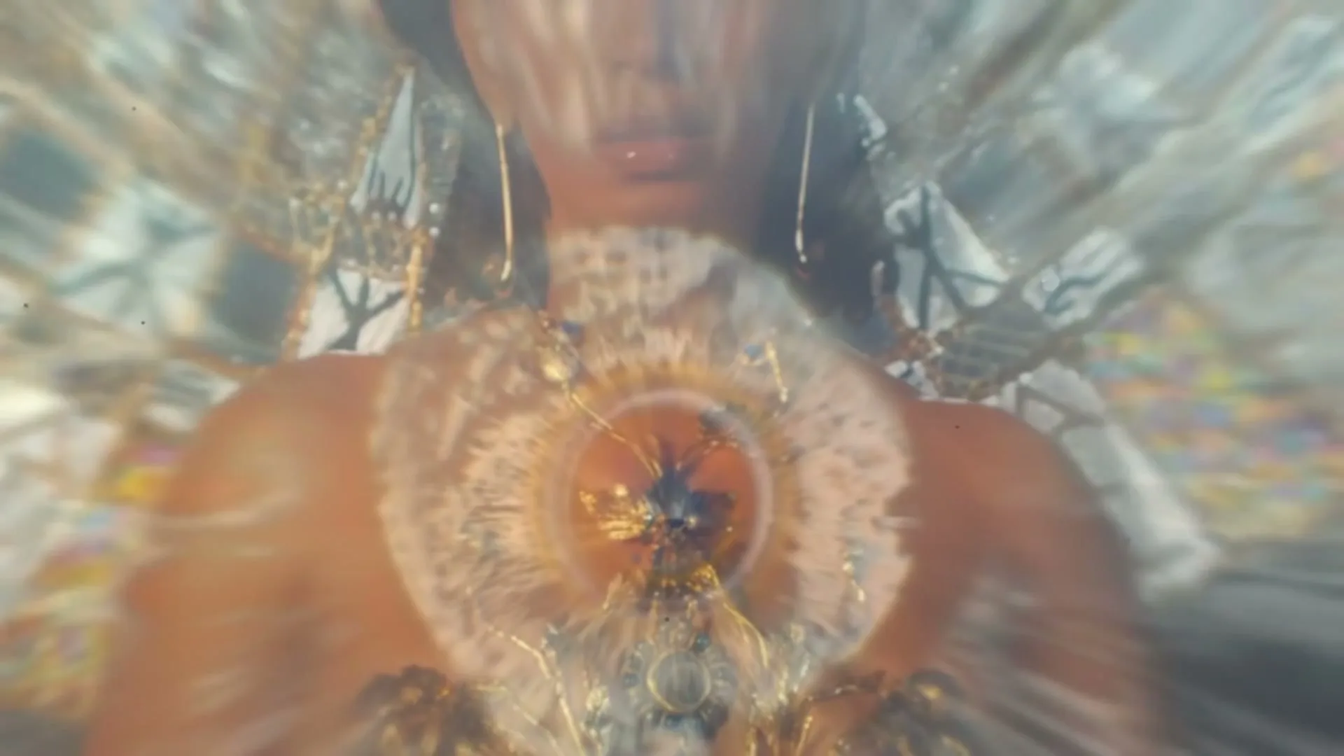 A woman with dark skin and hair, wearing a golden necklace, looks directly at the camera as the background transitions from a kaleidoscope to a cosmic explosion.