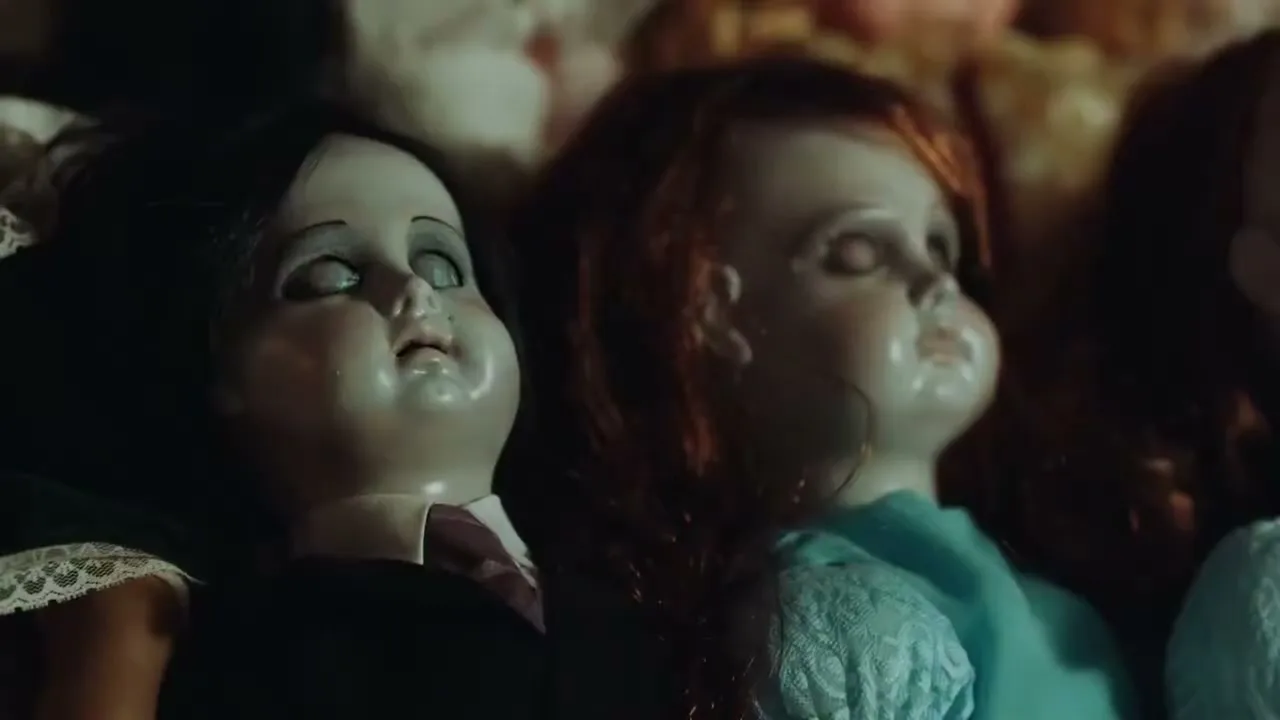 A closeup shot of two vintage dolls, one with dark hair and a suit, the other with red hair and a blue dress, lying among other dolls.