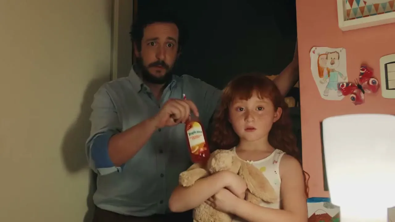 A father and his young daughter stand in a doorway, looking surprised; the father drinks from a Tropicana bottle while the daughter holds a stuffed animal.