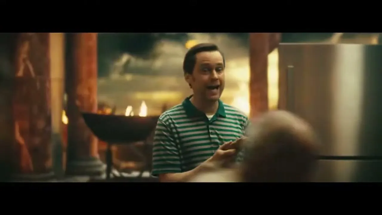 A man in a striped shirt tries to hand a hot dog to people fleeing a collapsing, burning building, while he stands in a modern kitchen.