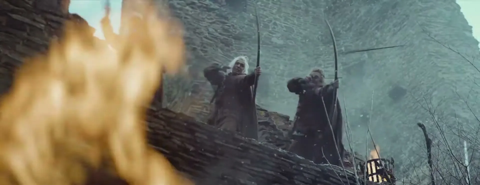 Two male archers with long white hair and beards aim their bows from a stone castle wall, with fire in the foreground.