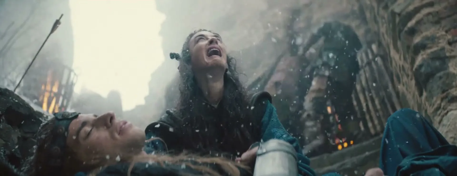 A female elf in blue and brown clothing holds a dying male elf in a battle-torn, snowy fantasy landscape, looking up and screaming in anguish.