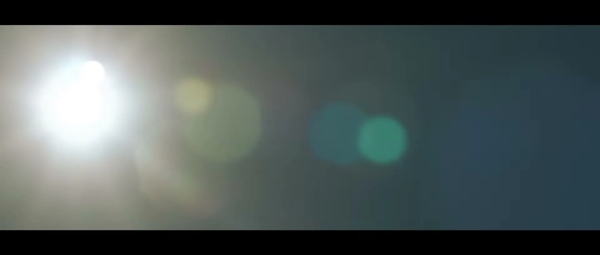A bright lens flare from the sun dominates the left side of the frame, with colorful bokeh effects visible against a dark background.