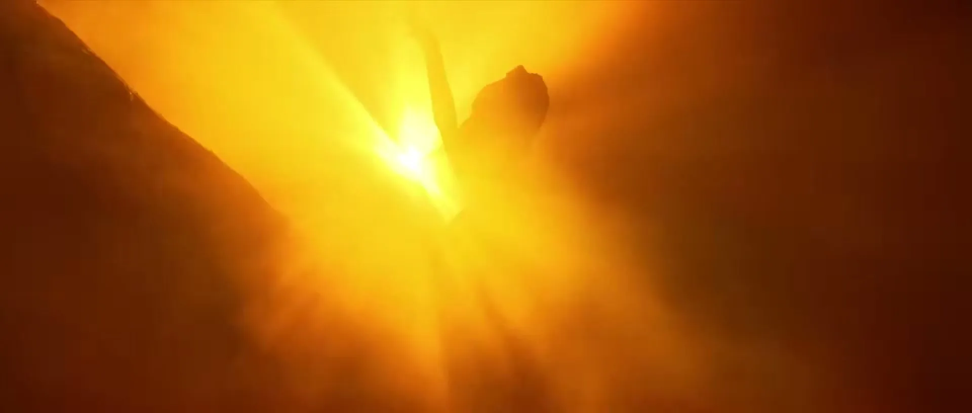 A female model in silhouette poses with arms raised against a bright, sun-like light source in a hazy, orange-lit environment.