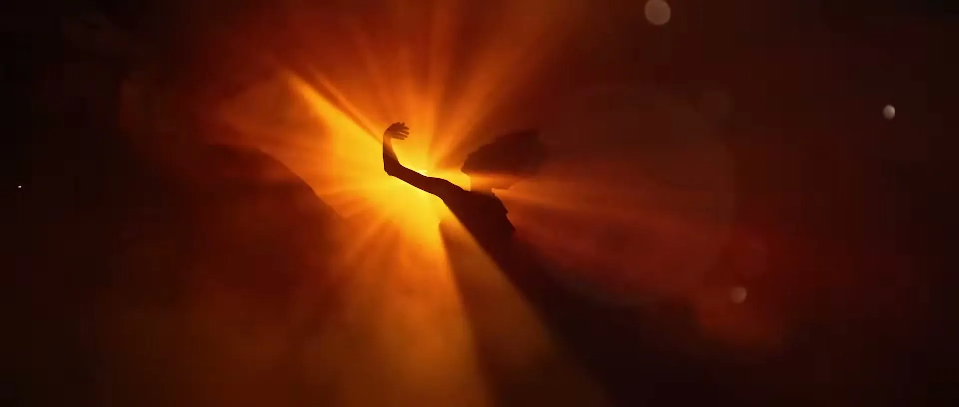 A silhouetted woman with her arm raised is bathed in bright orange light, creating a dramatic and ethereal scene.